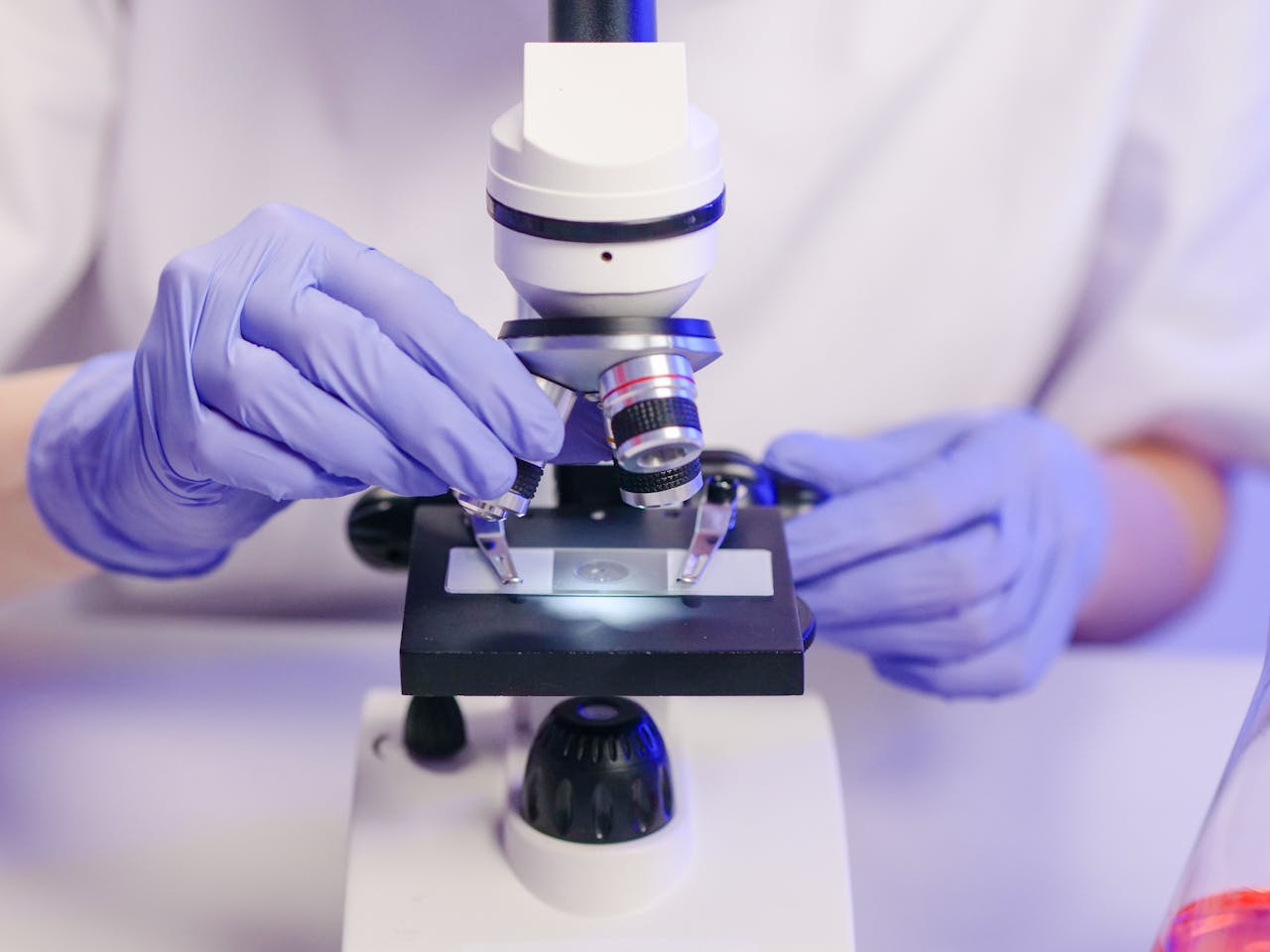 Scientist wearing gloves using a microscope in a laboratory setting.